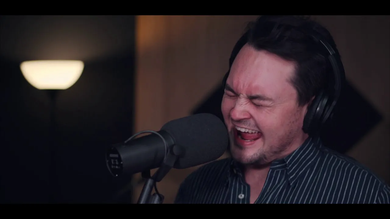 Man wearing headphones singing passionately into a microphone in a dimly lit room.