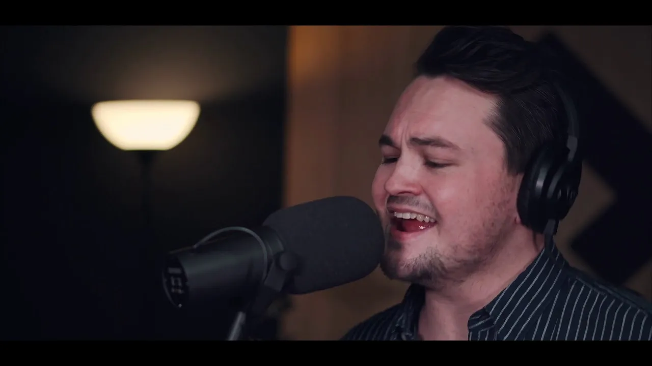 Man wearing headphones singing into a professional microphone with a blurred lamp in the background.
